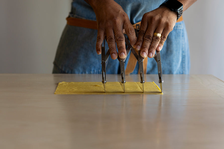 Cutting a sheet of fresh pasta dough with a pasta cutter at a Pasta Packs pasta making class in Tampa